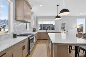 Kitchen with dual tone cabinetry, stainless steel range with gas stovetop, hanging light fixtures, light wood finished floors, and a kitchen bar
