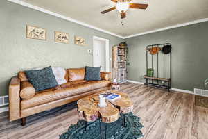 Living area featuring a textured ceiling, wood finished floors, a ceiling fan, ornamental molding, and a textured wall