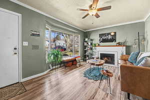 Living room with a textured ceiling, ceiling fan, wood finished floors, crown molding, and a fireplace