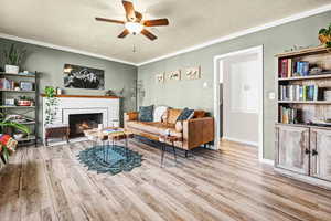 Living room with a textured ceiling, a tiled fireplace, a textured wall, ceiling fan, and light wood-style floors