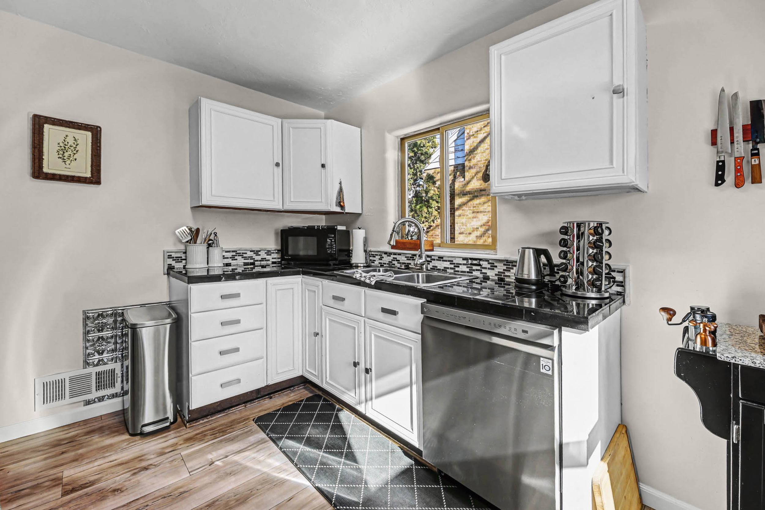 Kitchen featuring dark countertops, stainless steel dishwasher, white cabinetry, and wood finish floors