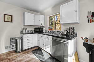 Kitchen featuring dark countertops, stainless steel dishwasher, white cabinetry, and wood finish floors