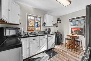 Kitchen with white cabinetry, dark countertops, stainless steel appliances, and light wood-type flooring