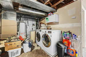 Laundry room with unfinished concrete floors, water heater, heating unit, separate washer and dryer, and cabinet space