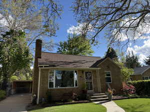 View of front facade with a chimney, a front yard, brick siding, driveway, and a shingled roof