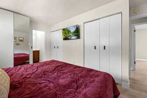 Bedroom featuring light wood finished floors, a textured ceiling, and two closets