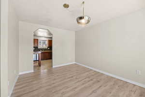 Unfurnished living room featuring arched walkways, light wood-style floors, and a textured ceiling