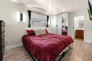 Bedroom with light wood finished floors, a textured ceiling, a closet, and ensuite bath