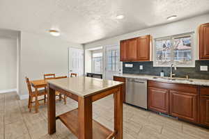 Kitchen with light stone countertops, a textured ceiling, dishwasher, tasteful backsplash, and wood finish cabinets