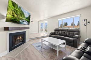 Living area with a warm lit fireplace, a textured ceiling, and light wood finished floors