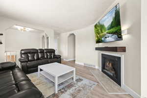 Living room with light wood-style flooring, a lit fireplace, arched walkways, and a textured ceiling