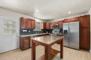 Kitchen featuring stainless steel appliances, wood finish cabinets, light stone countertops, recessed lighting, and backsplash