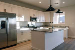 Kitchen featuring stainless steel appliances, white cabinetry, dark stone countertops, and light wood-style floors