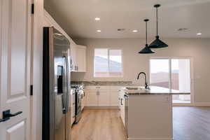 Kitchen with stainless steel appliances, white cabinetry, light wood-style flooring, and a center island with sink