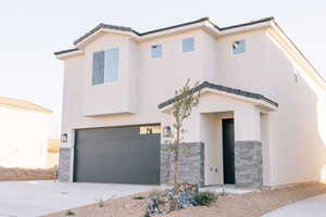 View of front of house with stone siding, a garage, concrete driveway, and stucco siding