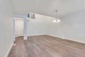 Empty room with light wood-style flooring and suspended lighting