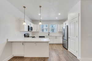 Kitchen featuring a peninsula, stainless steel appliances, pendant lighting, white cabinetry, and a textured ceiling