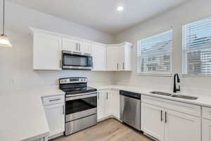 Kitchen featuring stainless steel appliances, white cabinetry, light wood-type flooring, and pendant lighting