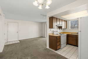 Kitchen featuring white appliances, light countertops, light tile patterned floors, light carpet, and suspended lighting