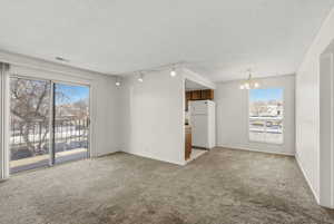 Unfurnished room featuring light carpet, a textured ceiling, and a chandelier