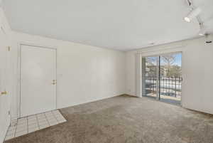 Carpeted empty room featuring a textured ceiling, rail lighting, and tile patterned floors