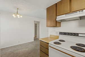 Kitchen with white electric stove, wood finish cabinets, light countertops, a chandelier, and a textured ceiling
