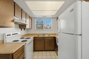 Kitchen with white appliances, light countertops, wood finish cabinetry, and light tile patterned floors