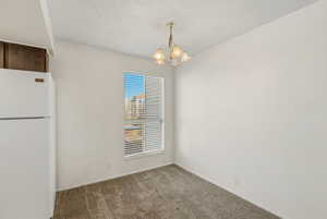 Unfurnished dining area featuring carpet, suspended lighting, and a textured ceiling