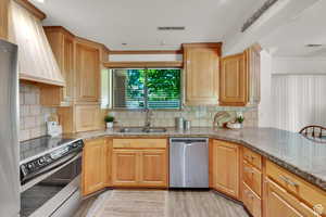 Kitchen with stainless steel appliances, light stone counters, ornamental molding, light wood-type flooring, and decorative backsplash