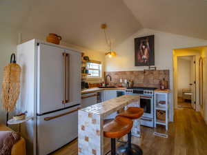 Kitchen featuring white appliances, pendant lighting, dark wood finished floors, and a breakfast bar area