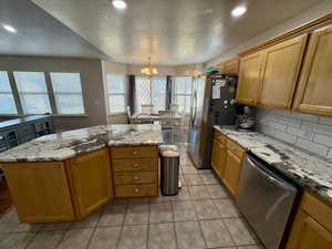 Kitchen featuring stainless steel appliances, wood finish cabinetry, light stone countertops, a textured ceiling, and light tile patterned floors