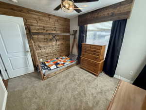 Carpeted bedroom with wooden walls and ceiling fan