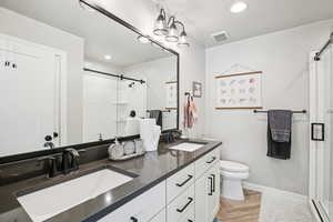 Bathroom featuring a shower stall, double vanity, parquet flooring, and recessed lighting