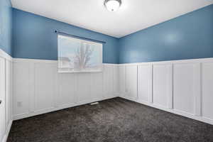 Unfurnished room featuring a decorative wall, wainscoting, and dark colored carpet