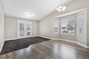 Spare room featuring wood finished floors, lofted ceiling, french doors, and hanging lights