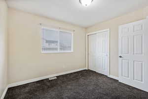 Unfurnished bedroom featuring dark carpet and a closet