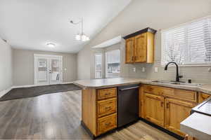 Kitchen featuring lofted ceiling, decorative backsplash, light wood finished floors, dishwasher, and light countertops