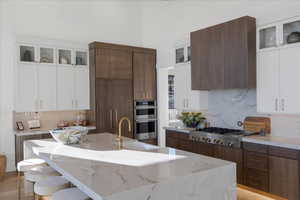 Kitchen featuring dual tone cabinets, glass insert cabinets, backsplash, light wood-style floors, and light stone counters