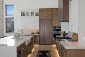 Kitchen featuring two tone color scheme, glass fronted cabinets, light wood-style floors, stainless steel appliances, and tasteful backsplash