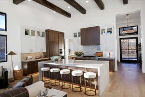 Two tone kitchen with two tone cabinetry, glass fronted cabinets, a breakfast bar area, light wood-type flooring, and light stone counters