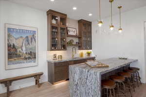 Bar featuring light wood-type flooring, decorative light fixtures, decorative backsplash, and glass insert cabinets