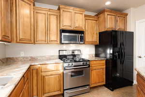 Kitchen with stainless steel appliances, light stone countertops, recessed lighting, wood finish cabinets, and light tile patterned floors