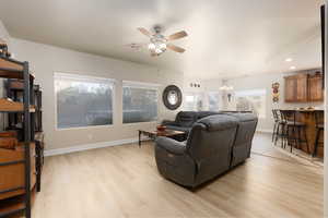 Living room with light wood-type flooring, ceiling fan, and suspended lighting