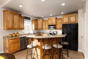 Kitchen with stainless steel appliances, a kitchen breakfast bar, light stone countertops, recessed lighting, and a center island