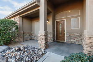Doorway to property featuring stone siding, covered porch, and stucco siding