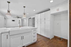 Kitchen featuring white cabinetry, decorative light fixtures, ceiling fan, light stone countertops, and dark wood finished floors