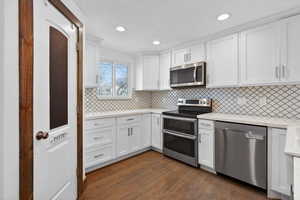 Kitchen with stainless steel appliances, white cabinets, dark wood-type flooring, light stone countertops, and recessed lighting