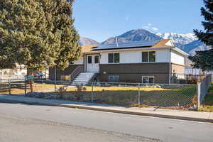 View of front of property with brick siding, a mountain view, a fenced front yard, and solar panels