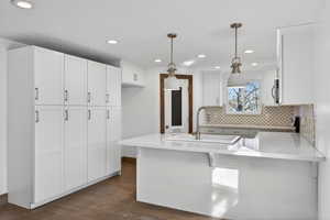 Kitchen with a peninsula, light stone countertops, hanging light fixtures, a kitchen bar, and white cabinets