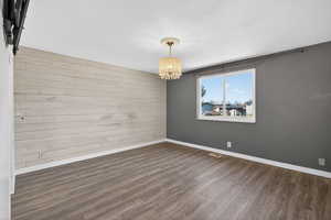 Unfurnished room featuring wood walls, wood finished floors, suspended lighting, and an accent wall